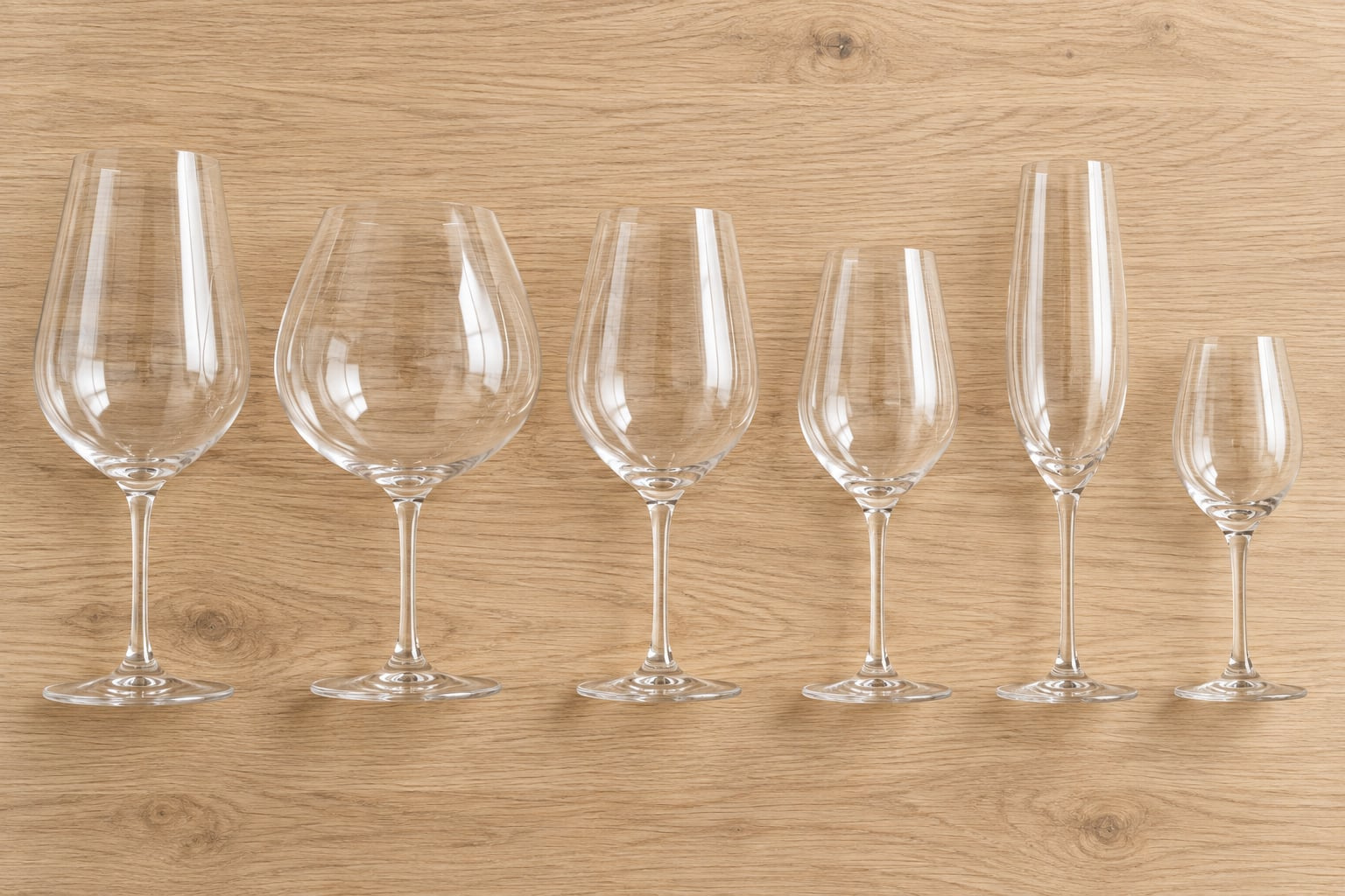 Six empty wine glasses with different bowl shapes arranged on a wooden surface