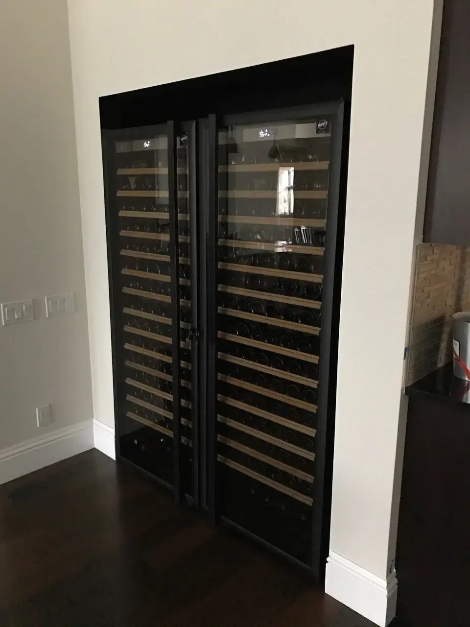 Built-in glass-door wine fridge with dark wood floor and wall outlets nearby.