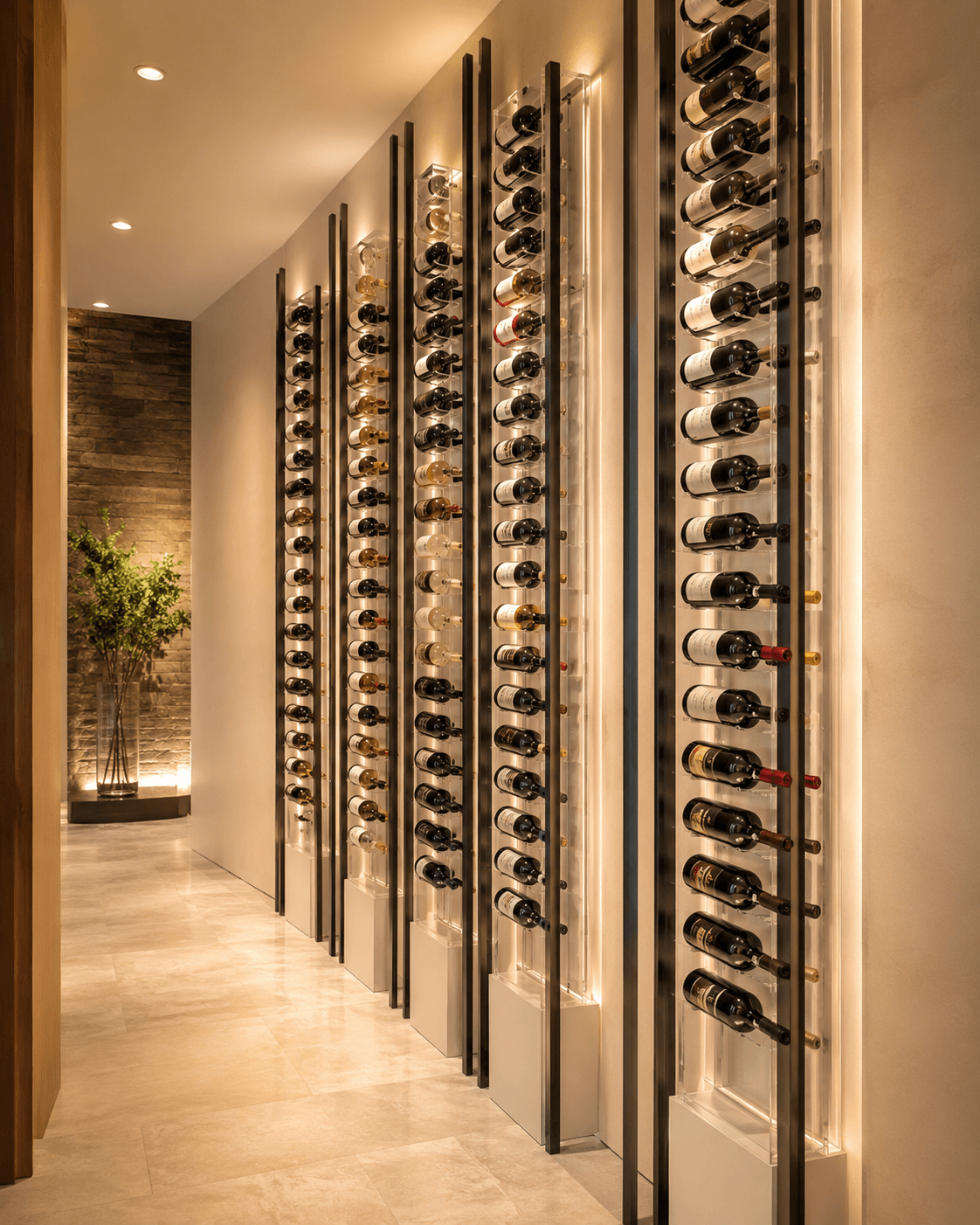Modern commercial wine cellar with illuminated vertical racks displaying multiple bottles of wine along a hallway with light-colored floors and walls. Tall plant in the background.